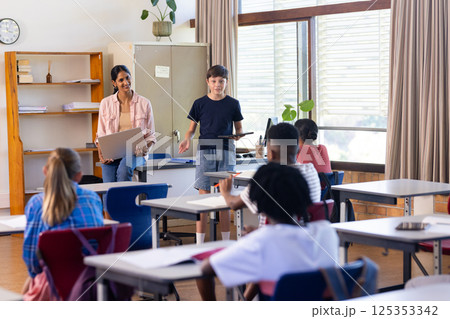 In school, Indian female teacher and student presenting with laptop in classroom to peers In school, Indian female teacher and student presenting with laptop in classroom to peers 125353342