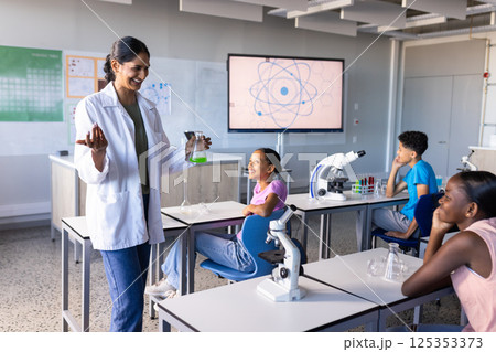 In school, Indian female teacher conducting science experiment with students in classroom 125353373