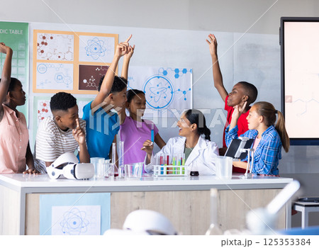 In school, students raising hands and engaging with Indian female teacher in science classroom 125353384