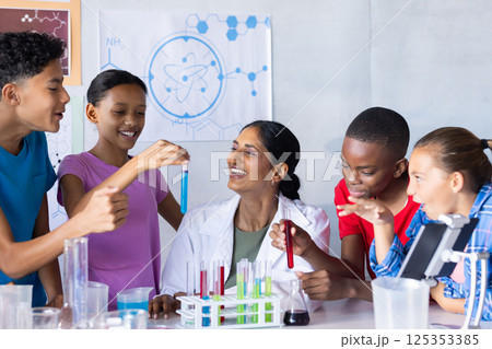 In school, students conducting science experiment with Indian female teacher, holding test tubes 125353385