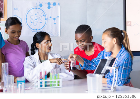 In school, Indian female teacher and students conducting science experiment with test tubes 125353386