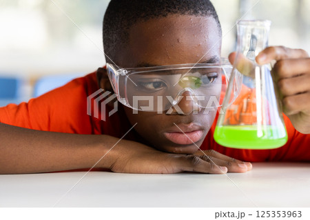 In school, boy examining green liquid in flask during science experiment In school, boy examining green liquid in flask during science experiment 125353963
