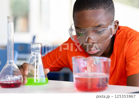 In school, boy conducting science experiment with beakers and safety goggles In school, boy conducting science experiment with beakers and safety goggles 125353967