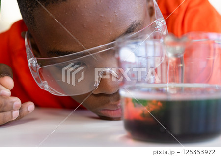Conducting science experiment, boy wearing safety goggles observing liquid in school Conducting science experiment, boy wearing safety goggles observing liquid in school 125353972