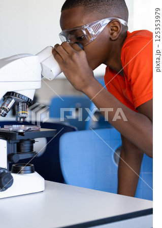 In school, boy using microscope and wearing safety goggles in science classroom 125353979