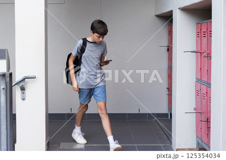 Walking in school hallway, boy with backpack using smartphone near lockers Walking in school hallway, boy with backpack using smartphone near lockers 125354034