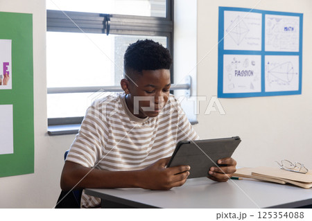 In school, boy using tablet at desk, focusing on screen 125354088