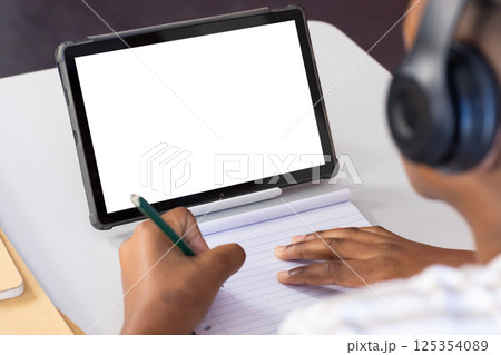 Using tablet and writing in notebook, student studying in school classroom, copy space 125354089