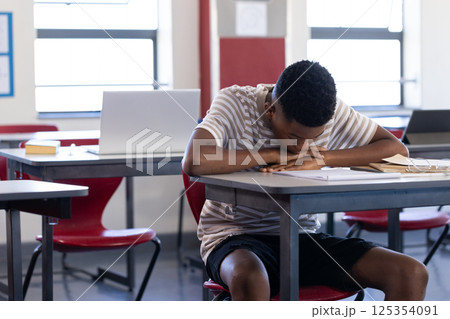 In school, boy resting head on desk in classroom, looking tired In school, boy resting head on desk in classroom, looking tired 125354091