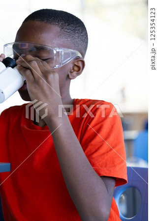 Using microscope, boy in school wearing safety goggles, focusing on experiment 125354123