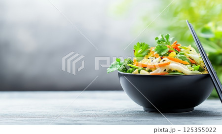 Fresh vegetable stir fry in black bowl on rustic table with chopsticks 125355022