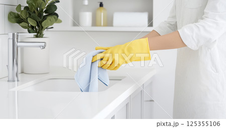 Female cleaning kitchen sink with yellow gloves in modern home Female cleaning kitchen sink with yellow gloves in modern home 125355106
