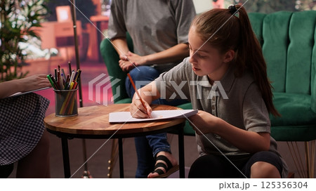 During a therapy session, an adolescent girl practices drawing to help with behavioral therapy and emotional regulation. The therapist and mother provide support for her mental wellbeing. Camera A. During a therapy session, an adolescent girl practices drawing to help with behavioral therapy and emotional regulation. The therapist and mother provide support for her mental wellbeing. Camera A. 125356304