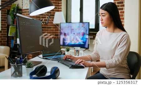 Professional software developer types code on a laptop in a sleek workspace. Asian female freelancer doing remote work on app development, software engineering and agile coding practices. Camera A. Professional software developer types code on a laptop in a sleek workspace. Asian female freelancer doing remote work on app development, software engineering and agile coding practices. Camera A. 125356317