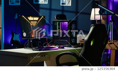 Professional gaming empty room studio with neon lights and RGB lit powerful computer, first person shooter game left open on screen. FPS videogame on pc display in apartment late at night 125356364