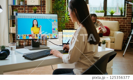 Asian graphic designer uses editing software for photo retouching in a well organized home workspace. Female freelancer uses digital tools essential for a creative artistic career. Camera A. Asian graphic designer uses editing software for photo retouching in a well organized home workspace. Female freelancer uses digital tools essential for a creative artistic career. Camera A. 125356377