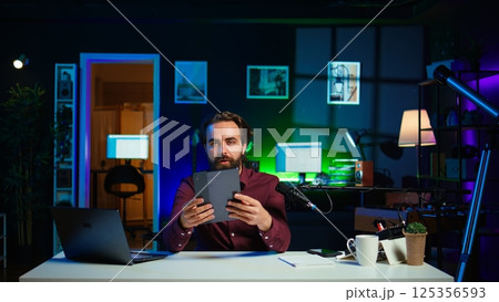 Tech expert presenting tablet in entry level low budget price range to interested viewers, filming in studio. Viral content creator reviewing digital device in front of internet audience, camera B 125356593