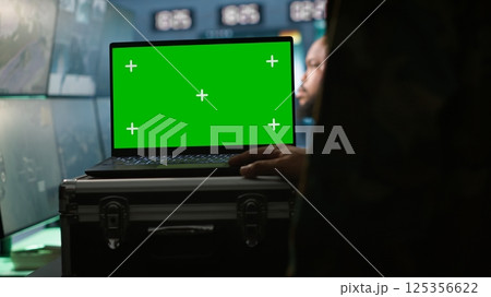 Military agent working in control room, using isolated screen software on laptop, analyzing aerial reconnaissance data. Intelligence corps expert controlling drones with mockup notebook, camera A 125356622