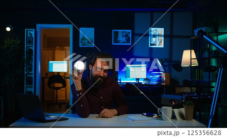 Entertainer using light bulb to create atmospheric mood while entertaining audience. Disheveled man in apartment using light to create spooky vibe, pretending to be electrocuted, camera B 125356628