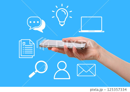 User interacts with mobile device amidst icons conveying communication and technology 125357334