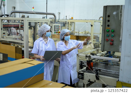 Factory workers overseeing automated packaging equipment in canned fish processing 125357422