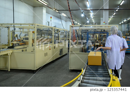 Factory workers overseeing boxed products on a conveyor belt in a canned fish Factory workers overseeing boxed products on a conveyor belt in a canned fish 125357441