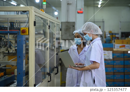 Factory workers overseeing automated packaging equipment in canned fish processing Factory workers overseeing automated packaging equipment in canned fish processing 125357477