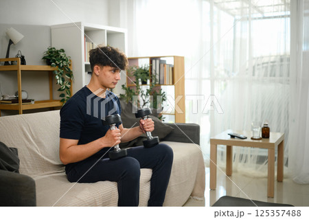Focused male doing arm workouts with dumbbells on a couch 125357488