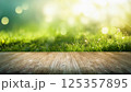 木製テーブル越しの日差しを浴びた緑の草原とボケ背景 125357895