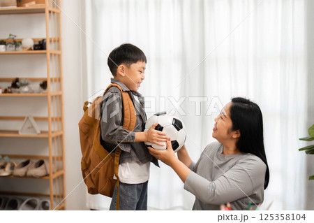 Back to School and Sports. A mother handing a soccer ball to her son after packing his backpack. 125358104