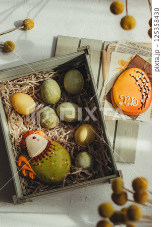 Close up of colorful Easter eggs in a wooden box, Easter cookies chicken and egg and decorations on the background, vintage style Close up of colorful Easter eggs in a wooden box, Easter cookies chicken and egg and decorations on the background, vintage style 125358430
