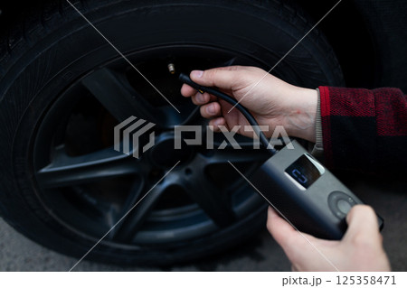 Close up of man hand holds a wireless portable air pump for inflating car tires. Self service, maintenance and safety.  125358471