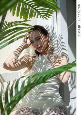 Beautiful brunette woman in summer sitting in the shade of a palm tree Beautiful brunette woman in summer sitting in the shade of a palm tree 125358700