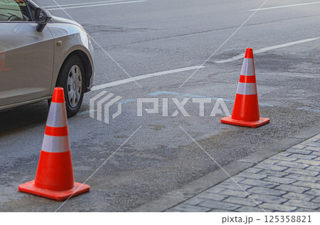 Empty parking place along on the side of a four-lane road with markings separating the directions of traffic, space for a car is reserved with orange and red plastic traffic cones 125358821