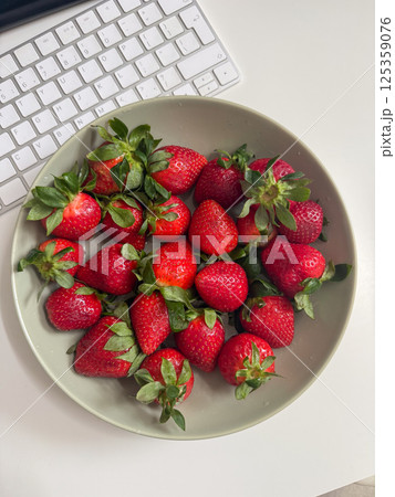 Fresh strawberries on a desk next to a keyboard. Digital lifestyle with healthy habits concept Fresh strawberries on a desk next to a keyboard. Digital lifestyle with healthy habits concept 125359076
