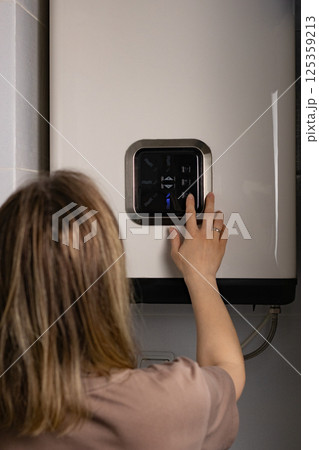 Cropped photo of female adjusting temperature on bathroom electric boiler hanging on wall, using control knob. Water heater in modern apartment Cropped photo of female adjusting temperature on bathroom electric boiler hanging on wall, using control knob. Water heater in modern apartment 125359213