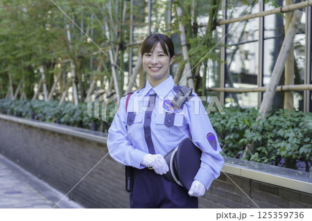 オフィスビルの前に立つ若い女性警備員　撮影協力：学校法人電波学園 東京電子専門学校 125359736