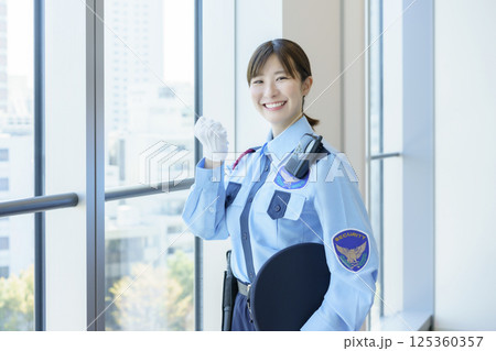 窓際に立つガッツポーズの若い女性警備員のポートレート　撮影協力：学校法人電波学園 東京電子専門学校 125360357