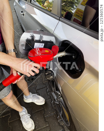 Trnava, Slovakia - 17.04.2025: Driver's hand holding fuel nozzle and filling car at gas station. Trnava, Slovakia - 17.04.2025: Driver's hand holding fuel nozzle and filling car at gas station. 125360574