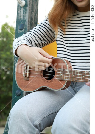 Girl Artist Hands Practices Playing The Ukulele In A Green Meadow 125360862