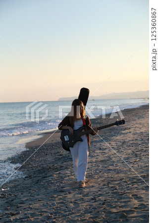 Girl Walks And Plays The Bass Instrument On The Beach Near The Ocean At Sunset Girl Walks And Plays The Bass Instrument On The Beach Near The Ocean At Sunset 125360867