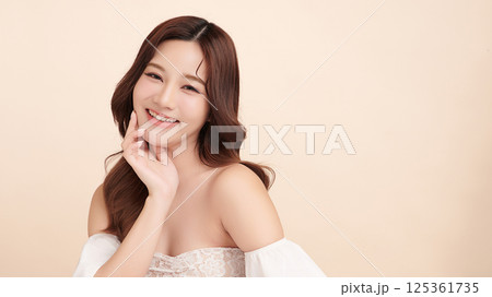 A beautiful young Asian woman with clean, fresh skin against a beige background. Skincare, facial treatment, cosmetology, beauty, and spa. An elegant portrait of an Asian woman. 125361735