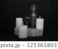 three burning candles on the oak stand with a glass and a bottle of homemade strong drink  125361803