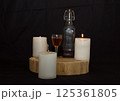 three burning candles on the oak stand with a glass and a bottle of homemade strong drink  125361805