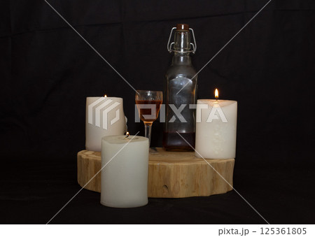 three burning candles on the oak stand with a glass and a bottle of homemade strong drink three burning candles on the oak stand with a glass and a bottle of homemade strong drink 125361805