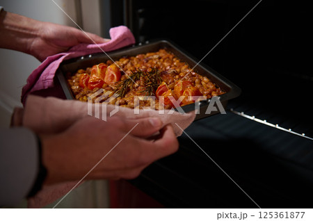 Home-cooked dish featuring baked beans with cherry tomatoes and rosemary, freshly taken out of the oven, capturing the warmth of homemade meals. Home-cooked dish featuring baked beans with cherry tomatoes and rosemary, freshly taken out of the oven, capturing the warmth of homemade meals. 125361877