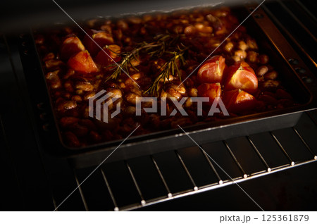 A baking dish filled with beans, tomatoes, and herbs is baking in an oven under warm light. The rustic preparation creates an inviting atmosphere, highlighting the freshness and simple cuisine. A baking dish filled with beans, tomatoes, and herbs is baking in an oven under warm light. The rustic preparation creates an inviting atmosphere, highlighting the freshness and simple cuisine. 125361879