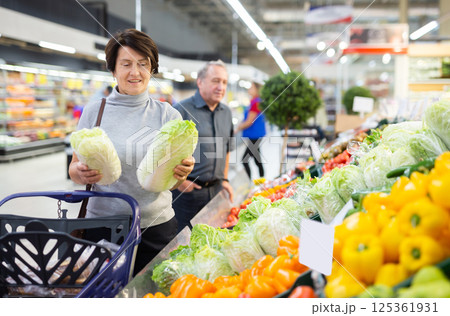 Mature female customer selects savoy cabbage with interest in grocery department of supermarket 125361931