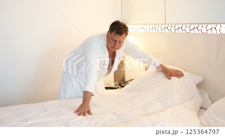 Morning chores, man in robe making bed after sleep, daily household duties 125364797