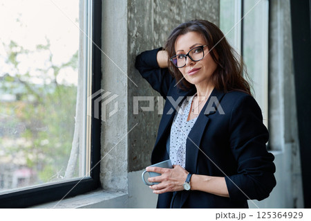 Portrait of middle aged beautiful businesswoman looking at camera, standing near window Portrait of middle aged beautiful businesswoman looking at camera, standing near window 125364929
